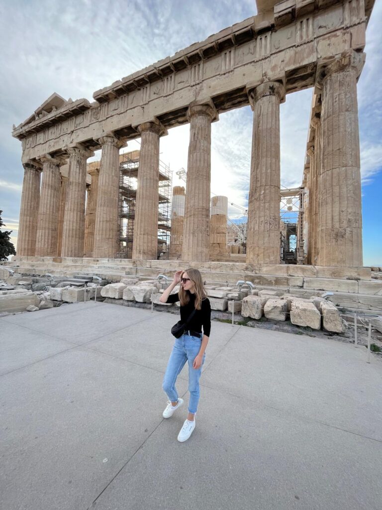 a BLOND GIRL STANDS IN FRONT OF ACROPOLIS ATHENS